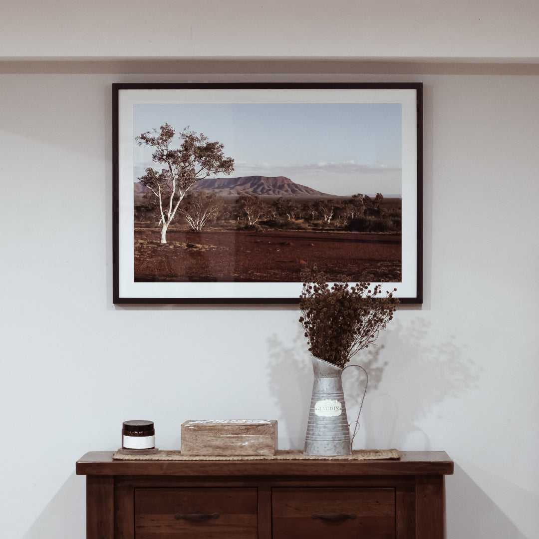 Karijini Australian landscape mountain photograph inside black print frame hanging over a brown table on a white wall