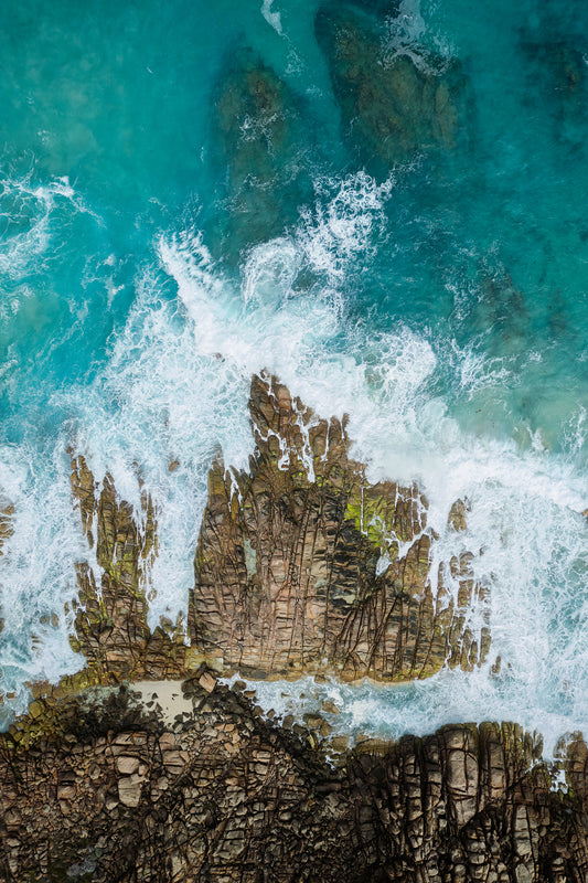 Aerial view of blue water and white wash smashing against rocks on the coastline